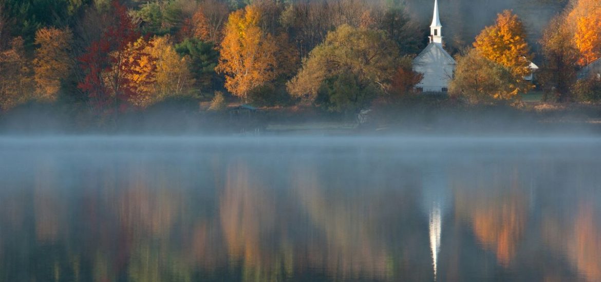 alberi con foglie di colore verde e arancione che si riflettono nelle acque di un lago in Vermont durante il foliage autunnale